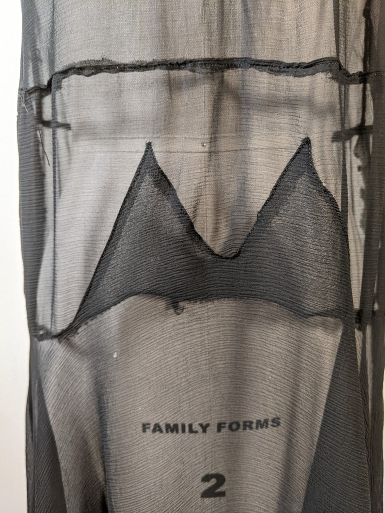 May include: Black sheer fabric with a black triangle shape sewn into the fabric. The fabric has a textured, woven look. The text "FAMILY FORMS 2" is visible at the bottom of the image.