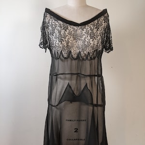 May include: A black sheer dress with a lace bodice and a scalloped hem. The dress is on a white mannequin and has the text "FAMILY FORMS 2 COLLAPSIBLE" printed on the skirt.