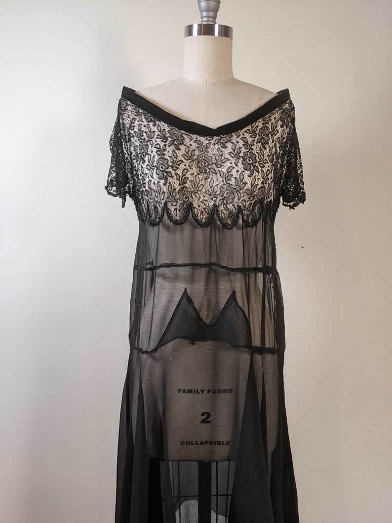 May include: A black sheer dress with a lace bodice and a scalloped hem. The dress is on a white mannequin and has the text "FAMILY FORMS 2 COLLAPSIBLE" printed on the skirt.