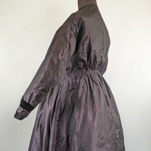 May include: A dark purple vintage coat with a high collar and long sleeves. The coat has a cinched waist and a full skirt. The sleeves have black velvet cuffs. The coat is made of a shiny, iridescent fabric.