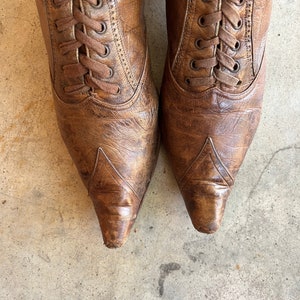 K&ouml;nnte beinhalten: Ein Paar braune Lederstiefel mit Schn&uuml;rung und spitz zulaufenden Zehen. Die Stiefel haben einen abgenutzten Look und sind mit braunen Schn&uuml;rsenkeln gebunden.
