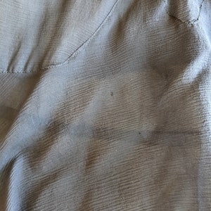 May include: Close-up of a dark gray fabric with a subtle textured pattern. The fabric is folded and has a seam running diagonally across the image.