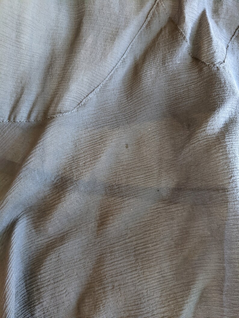 May include: Close-up of a dark gray fabric with a subtle textured pattern. The fabric is folded and has a seam running diagonally across the image.