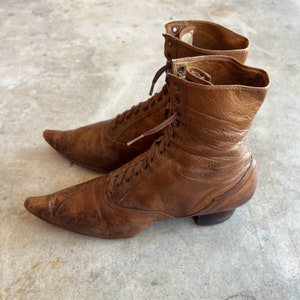 K&ouml;nnte beinhalten: Ein Paar braune Lederstiefel mit spitz zulaufenden Zehen und Schn&uuml;rungen. Die Stiefel haben einen Vintage-Look und sind in gutem Zustand.