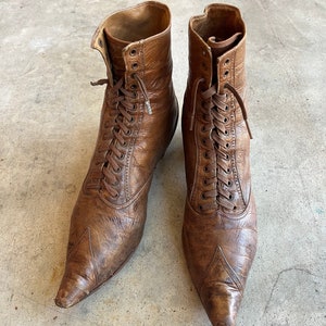 K&ouml;nnte beinhalten: Ein Paar braune Lederstiefel mit spitz zulaufenden Zehen und Schn&uuml;rung. Die Stiefel haben einen Vintage-Look und sind in gutem Zustand.