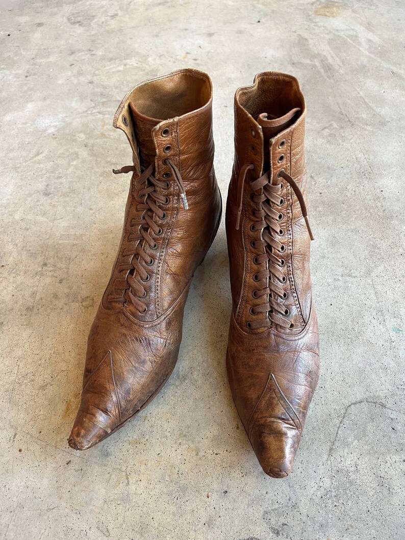 K&ouml;nnte beinhalten: Ein Paar braune Lederstiefel mit spitz zulaufenden Zehen und Schn&uuml;rung. Die Stiefel haben einen Vintage-Look und sind in gutem Zustand.