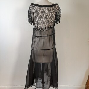 May include: A black sheer dress with a lace bodice and a scalloped hemline. The dress is on a mannequin and has a vintage style.
