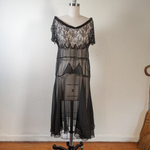 May include: A black sheer dress with a lace bodice and a scalloped hem. The dress is on a white background.