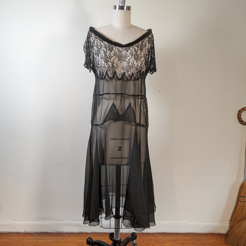 May include: A black sheer dress with a lace bodice and a scalloped hem. The dress is on a white background.