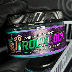 Op de afbeelding: Een ronde pot met een zwarte deksel die een blauwgroene substantie bevat. Het etiket heeft een paarse en groene afbeelding met een illustratie van bubble tea en de tekst MILKTEA.RC ROCKLOCK LOCK INTO THE LINE. De pot wordt tegen een donkere achtergrond gehouden.