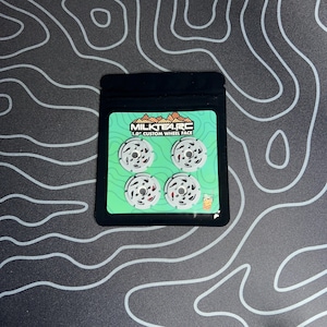 May include: A package containing four silver and red 1.0" custom wheel faces. The package has the text "MILKTEA.RC" and a graphic of a mountain range. The wheel faces are arranged in a square on a green background.