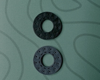 May include: Two circular, textured, dark gray and gray objects with a hole in the center. The objects have a repeating pattern of small, rounded rectangles around the outer edge and inner circle.