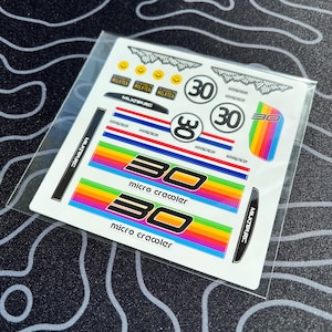 Pode incluir: Uma folha de autocolantes coloridos com vários desenhos. Os autocolantes incluem o número "30" em diferentes estilos, riscas arco-íris e o texto "micro crawler". Outros autocolantes apresentam o texto "MILKTEA" e "MILKTARC".