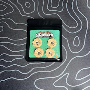 May include: A package containing four beige 1.0" custom wheel faces for RC vehicles. The package has a green backing with the text "MILKTEA.RC" and a graphic of a mountain range. The wheels have a circular design with multiple holes.
