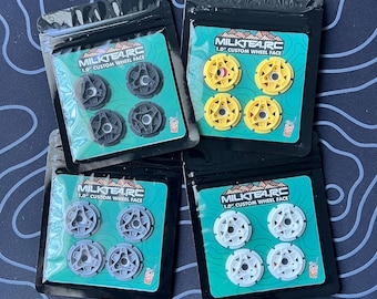 May include: Four sealed packages of custom wheel faces in various colors: gray, yellow, and white. Each package contains four wheel faces. The packages have a teal background with the text "MILKTEA.RC 1.0" CUSTOM WHEEL FACE".