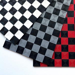 Op de afbeelding: Overzichtsfoto van drie getextureerde matten met een geometrisch vierkant patroon. Eén mat is zwart en wit, een andere is zwart en grijs, en de derde is zwart en rood. De matten overlappen elkaar en tonen de verschillende kleurencombinaties.