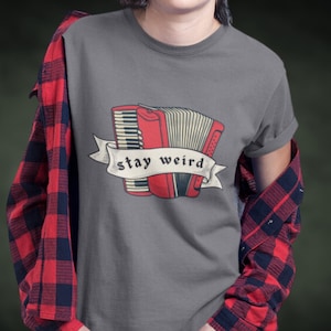 May include: A gray t-shirt with a red and black accordion illustration and the text "stay weird" in a banner.