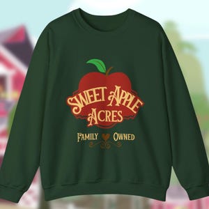 Puede incluir: Sudadera verde oscuro con un logotipo de manzana roja que dice "Sweet Apple Acres" en un estilo vintage. El texto "Family Owned" está debajo del logotipo. La sudadera es de cuello redondo.