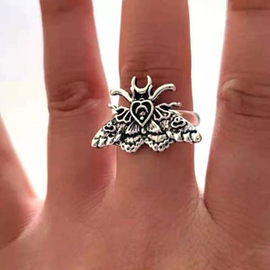 May include: A silver ring featuring a detailed moth design with a heart in the center.