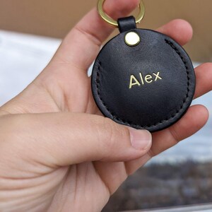 May include: A black leather keychain with a gold ring and the name "Alex" engraved in gold lettering.