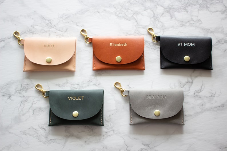 May include: Five small leather keychains with gold clasps and a snap closure. The keychains are personalized with the names "Maria", "Elizabeth", "#1 MOM", "VIOLET", and the date "09.21.2019".