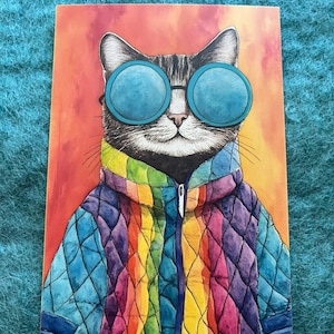 May include: A rectangular print featuring a stylized illustration of a tabby cat wearing large, round, blue-tinted sunglasses and a quilted, rainbow-colored zip-up jacket. The background is a warm, blended gradient of orange, red, and yellow tones.