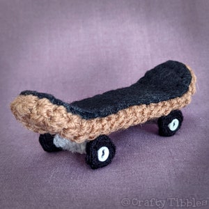 May include: A small crocheted skateboard with brown and black wheels. The deck is black felt and the trucks are brown yarn.