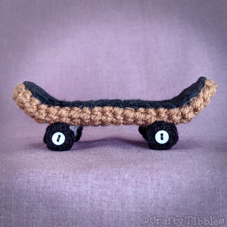 May include: A small crocheted skateboard with brown and black yarn. The skateboard has two black wheels with white centers.