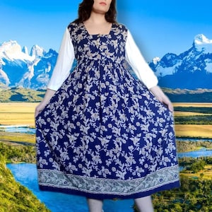 May include: A blue and white floral print midi dress with a white top and a gathered skirt. The dress has a square neckline and a button closure at the front. The model is wearing the dress with black boots.