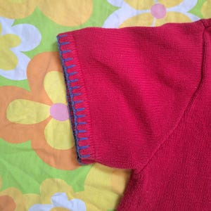 May include: Red short-sleeved knitted sweater with blue trim around the sleeves.