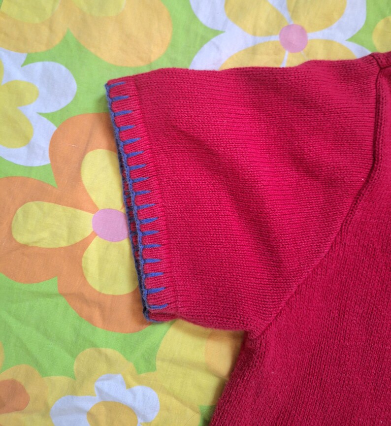 May include: Red short-sleeved knitted sweater with blue trim around the sleeves.
