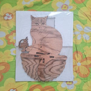 May include: A wooden cutout of a cat sitting on a shelf with a small bird cutout next to it. The cat is brown and the bird is light brown.