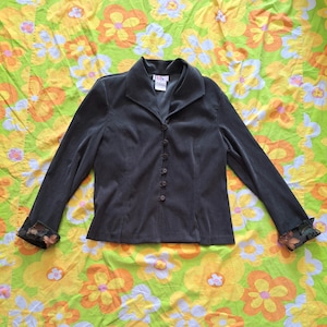 Może przedstawiać: Czarny blazer z kołnierzem i zapięciem na guziki. Blazer ma brązowe guziki i ozdobne wykończenia z tkaniny na mankietach.