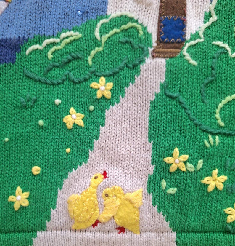 May include: A knitted fabric with a green background and a white path. The path has two yellow embroidered chicks facing each other. There are yellow embroidered flowers throughout the fabric.