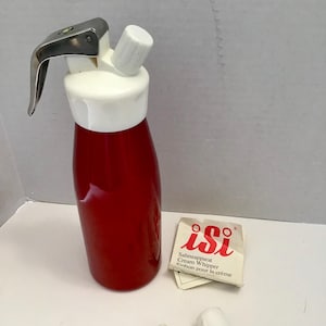 May include: A red and white cream whipper with a stainless steel lever. The whipper includes a white nozzle and a small instruction card. The whipper is designed for making whipped cream.