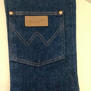 May include: A denim Christmas stocking with a Wrangler pocket design. The stocking is made of dark blue denim with copper rivets and a brown leather patch with the Wrangler logo. The pocket has a classic W-shaped stitching.