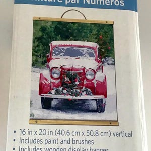 May include: Paint-by-Number Kit featuring a red vintage truck in a snowy scene. The kit includes paint, brushes, and a wooden display hanger. The finished painting is 16 x 20 inches (40.6 x 50.8 cm).