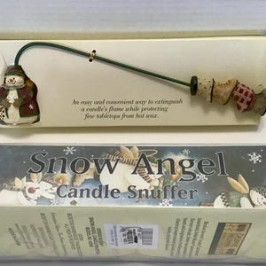 May include: A decorative candle snuffer with a snowman figure and a green handle. The snuffer is designed to extinguish candle flames. The packaging reads "Snow Angel Candle Snuffer".