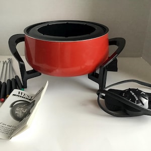 May include: A red West Bend electric fondue pot with black handles and a black base. Includes a set of fondue forks with colored tips and a user manual. The pot has a black interior and a power cord.
