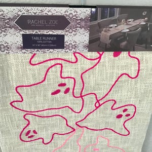May include: A beige table runner with a hot pink abstract design. The table runner is 16 x 90 inches and made of 100% cotton. The brand name "RACHEL ZOE" is visible on the packaging.