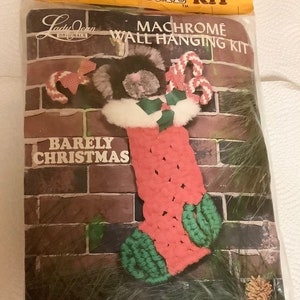 May include: A vintage craft kit for making a macrame stocking with a fuzzy, brown and white cat peeking out of the top. The kit includes polyolefin, polyester, acrylic fiber, a metal ring, felt, novelty eyes, ribbon, a pom pom, and complete instructions. The kit is called "Nifty Fuzzy Machrome Kit" and "Barely Christmas".