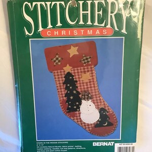 May include: A craft kit for making a Christmas stocking. The stocking is red and white with a plaid pattern and features a snowman, a tree, and stars. The kit includes fabric, batting, needles, thread, and instructions. The kit is from Bernat and is called "Stars in the Woods Stocking".