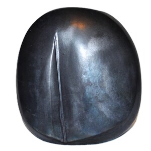 May include: A smooth, rounded, dark charcoal-coloured object with a matte finish. The surface features a single, vertical, slightly curved indentation or groove that runs from the top towards the bottom, creating a subtle texture on the otherwise plain, solid-coloured, pebble-like form.