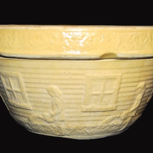 Może przedstawiać: Żółta ceramiczna miska do mieszania z wypukłym wzorem reliefowym na zewnątrz. Projekt przedstawia serię małych domków z oknami i otaczającym je listowiem, umieszczonych na tle poziomej, żebrowanej tekstury na korpusie miski.