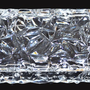 May include: A rectangular clear glass box featuring a highly textured, multifaceted geometric surface that creates a fractured, crystalline appearance. The lid and sides are composed of numerous angular, raised facets that reflect light.