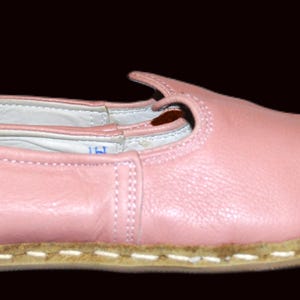 May include: A pair of pink leather ballet flats with a white stitched trim around the sole.