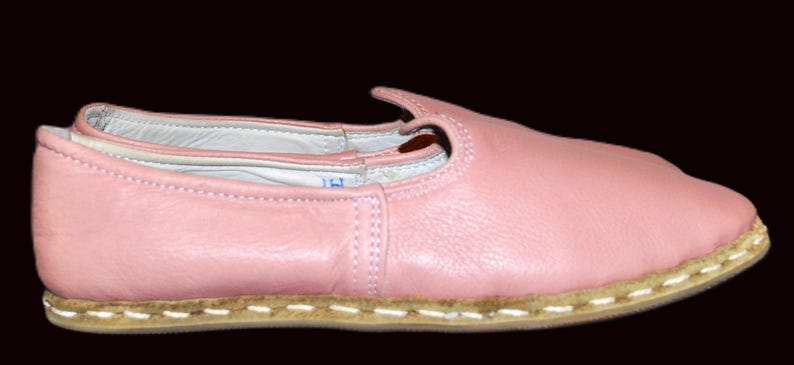May include: A pair of pink leather ballet flats with a white stitched trim around the sole.