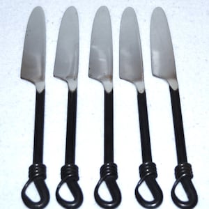Puede incluir: Juego de cinco cuchillos de cena de plata con mangos negros. Los mangos son de alambre retorcido y tienen un bucle en el extremo.