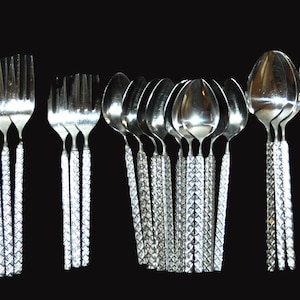 May include: A selection of silver cutlery, including knives, forks, and spoons, displayed on a black backdrop. The handles have a textured, geometric pattern. The set includes different sizes of spoons and forks.