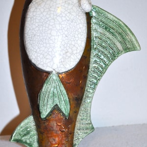 Op de afbeelding: Een keramische vaas in de vorm van een vis, met een witte, gecraqueleerde geglazuurde body en bruine, koperkleurige schubben. Groene vinnen en staart zorgen voor contrast. Een uniek decoratief item.
